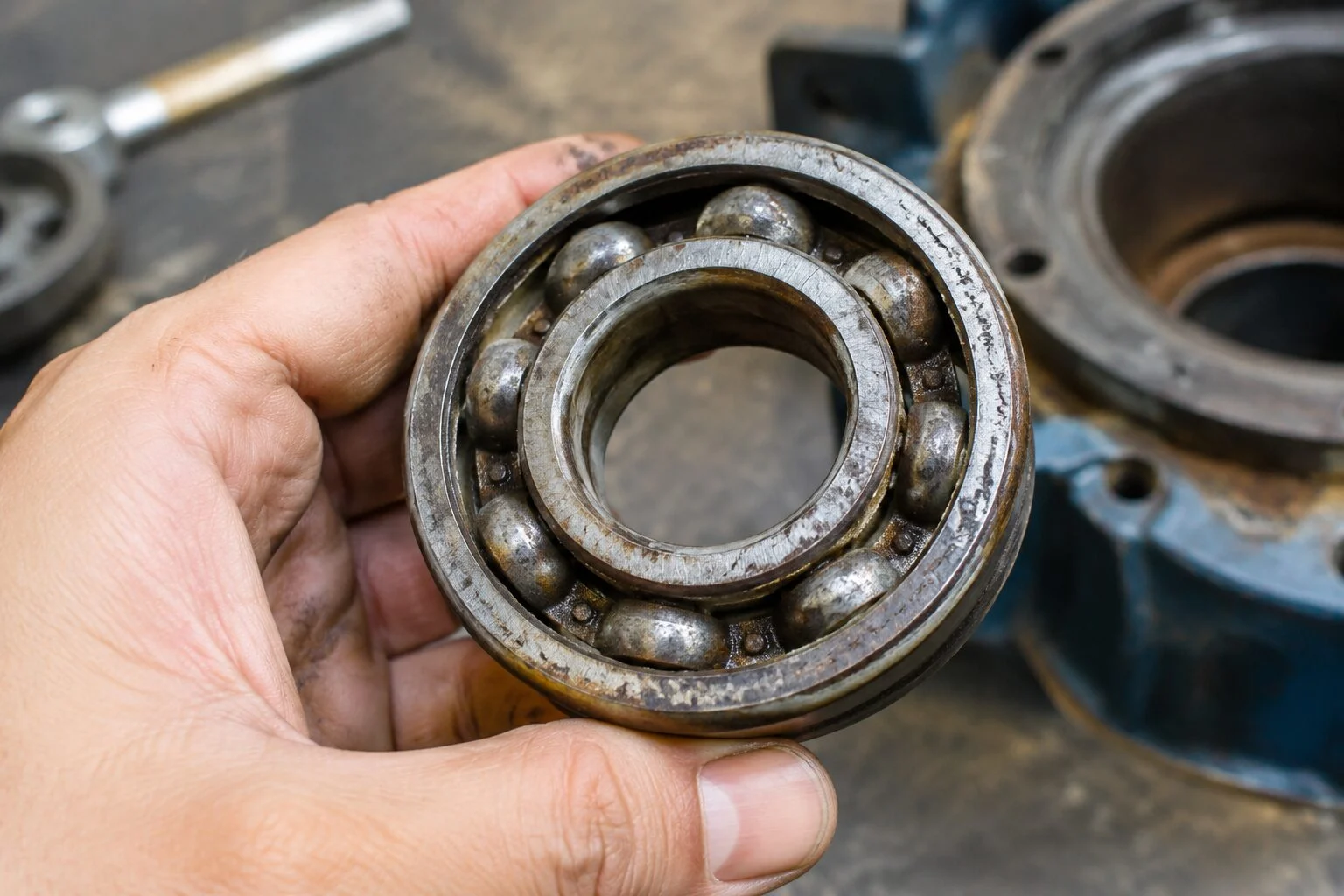 Worn industrial bearing with a faded steel stamp held in a technician's hand